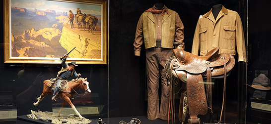 An exhibit in the National Cowboy & Western Heritage Museum, with clothes, a painting of a cowboy, a saddle, and a cowboy figurine